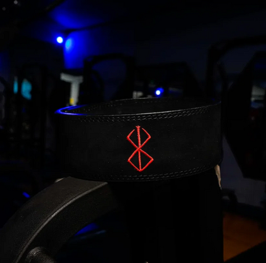 Embroidered powerlifting belt on gym equipment, black leather with red design, sturdy and durable.